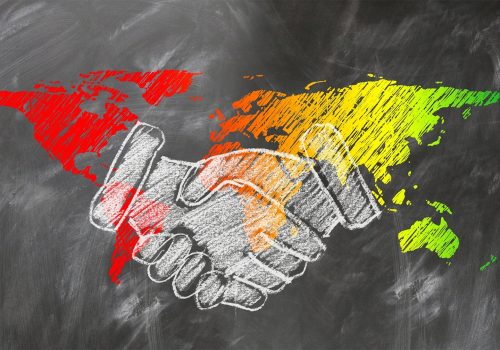 Shaking hands in front of world map drawn in chalk